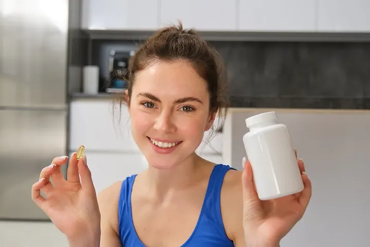 Woman holding iron supplement capsule and bottle