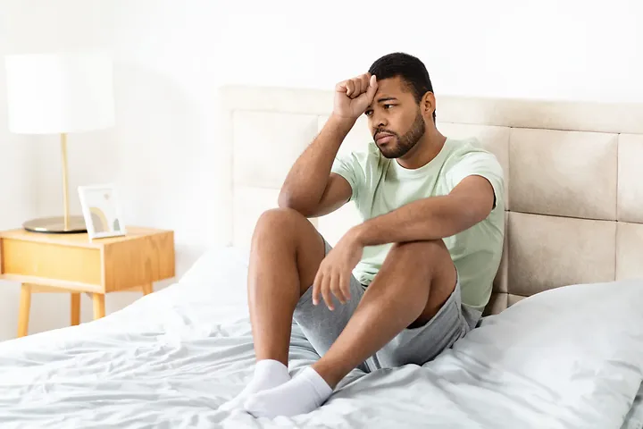 Man sitting on bed looking tired and stressed