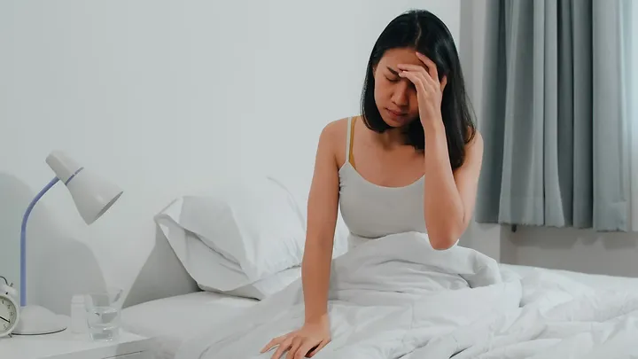 Tired woman sitting on bed with headache